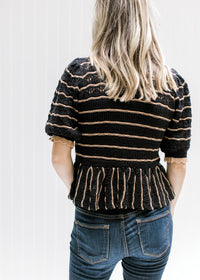 Back view of Model wearing a black sweater with rust stripes and a scalloping at neck and sleeve. 