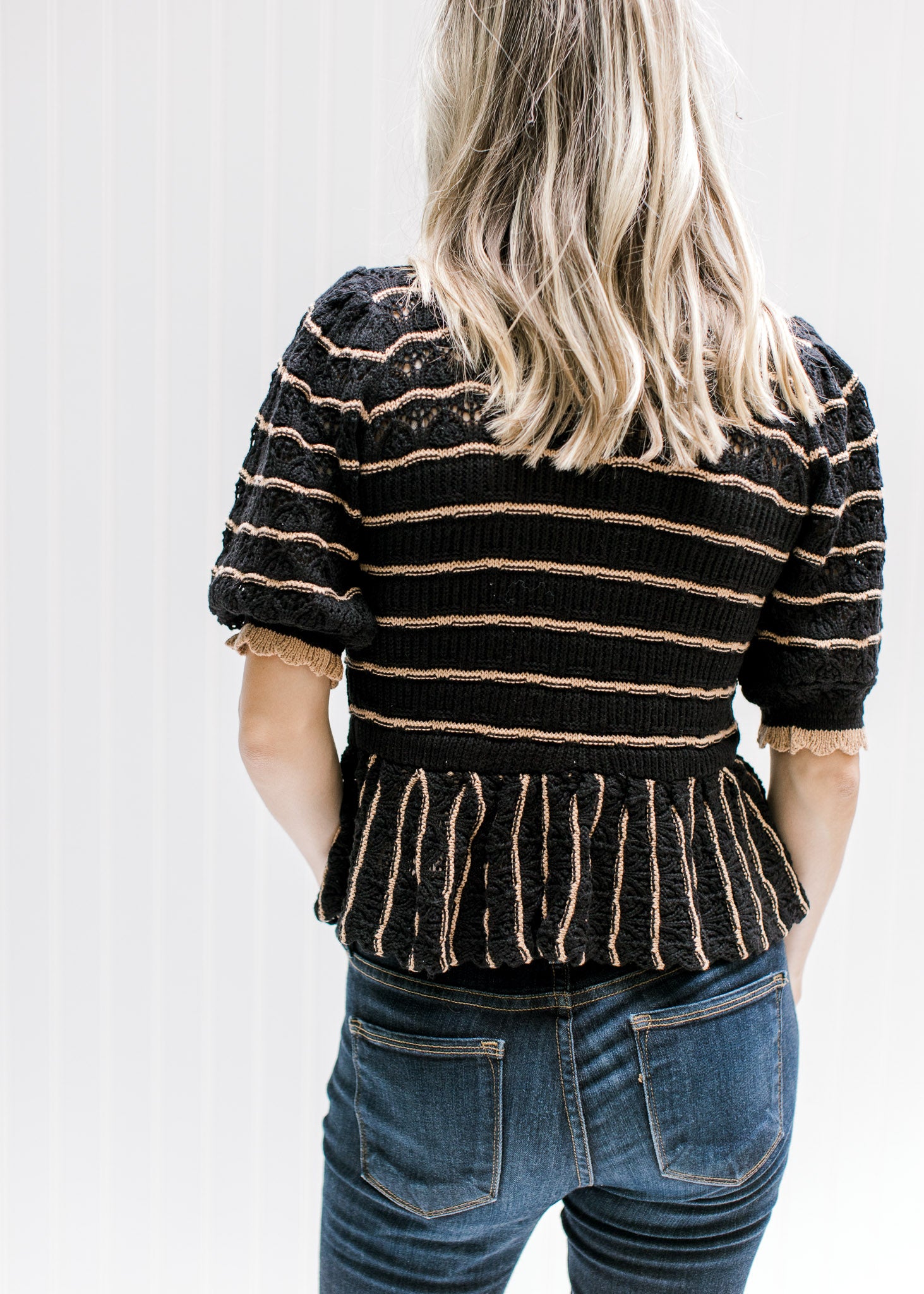 Back view of Model wearing a black sweater with rust stripes and a scalloping at neck and sleeve. 