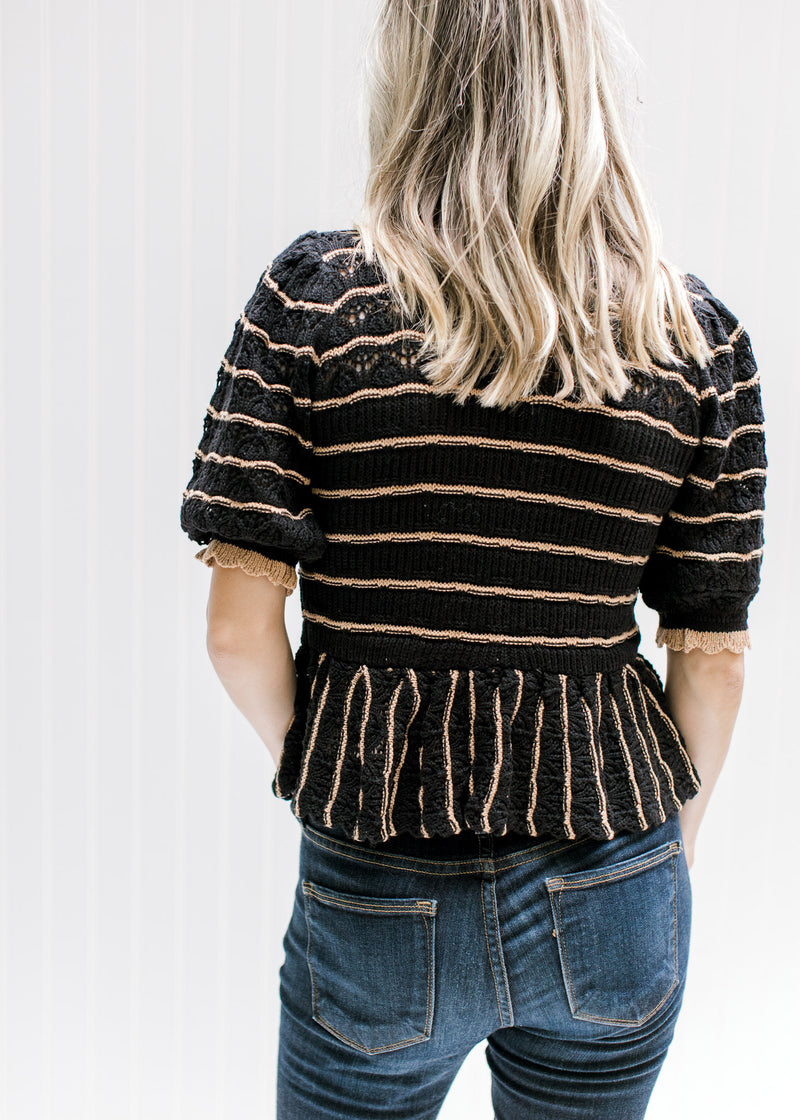 Back view of Model wearing a black sweater with rust stripes and a scalloping at neck and sleeve. 