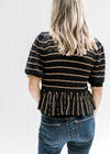 Back view of Model wearing a black sweater with rust stripes and a scalloping at neck and sleeve. 