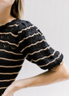 Detail view of scalloping detail on the sleeve of a black short sleeve sweater with rust stripes. 