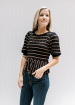 Model wearing jeans with a short sleeve black sweater with rust stripes and a scallop detail. 