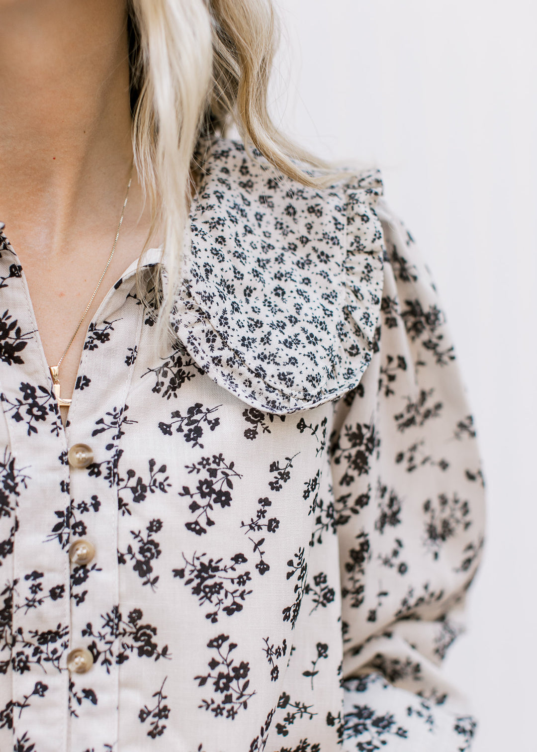 Close up of exaggerated collar and v-neck button front on a tan blouse with black microfloral. 