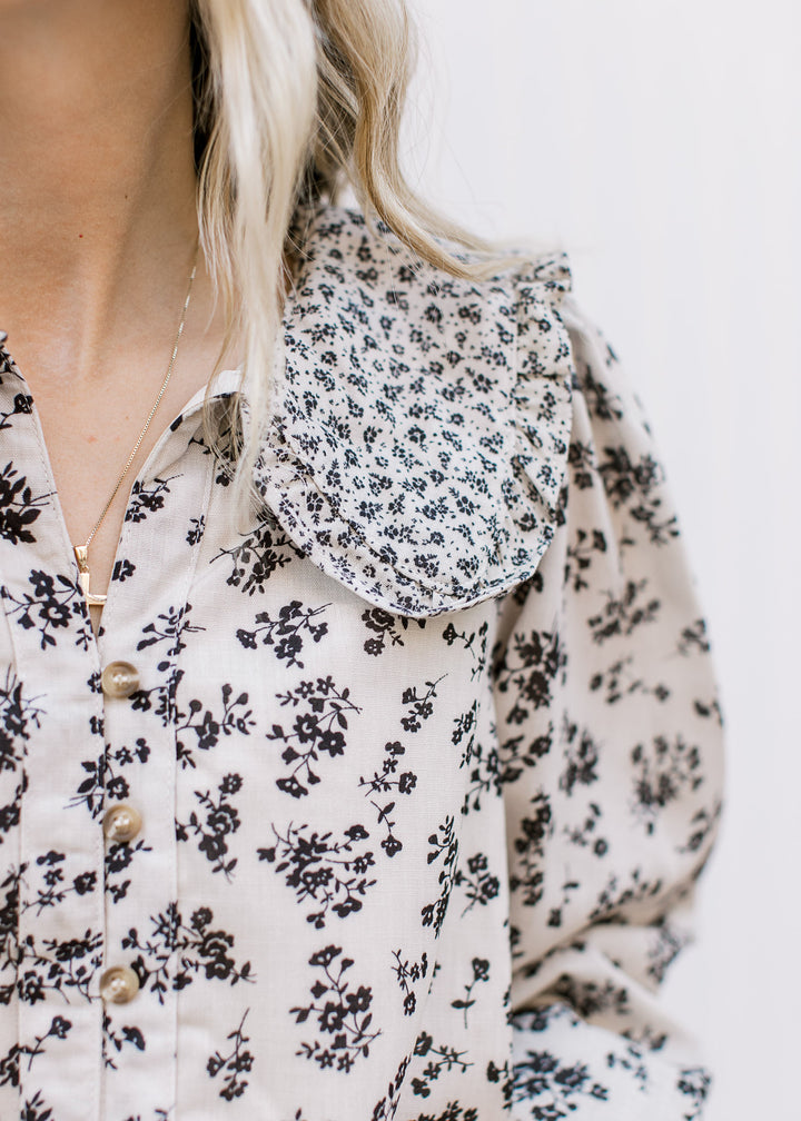 Close up of exaggerated collar and v-neck button front on a tan blouse with black microfloral. 