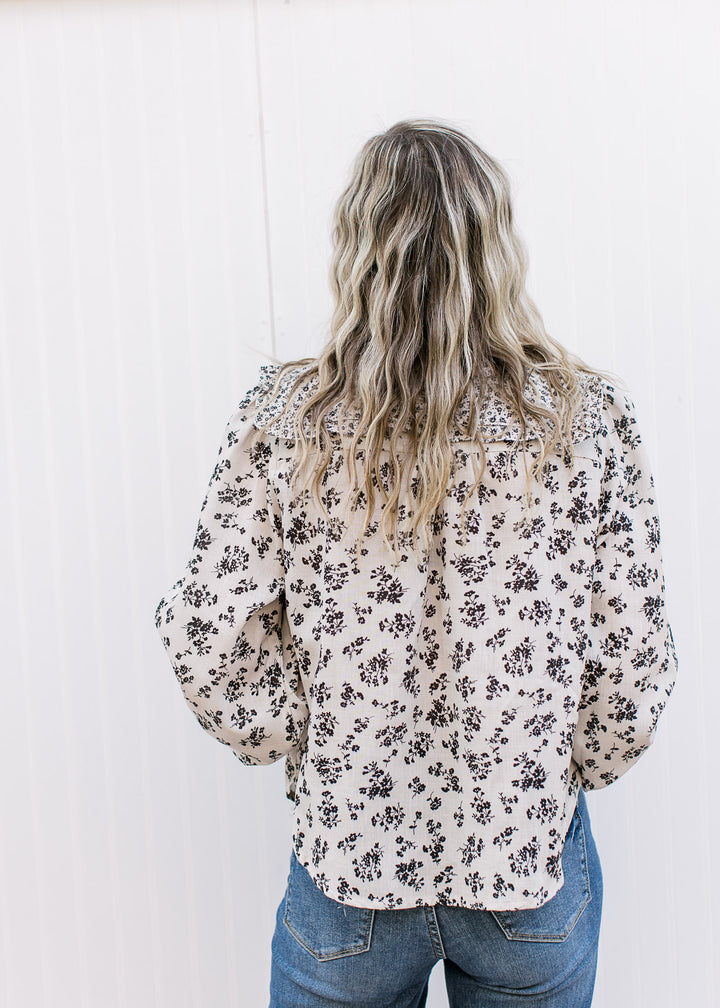 Back view of Model wearing a tan top with black microfloral, long sleeves and exaggerated collar.