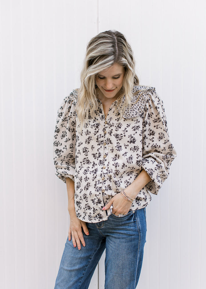Model wearing a tan button up top with black microfloral, long sleeves and exaggerated collar.