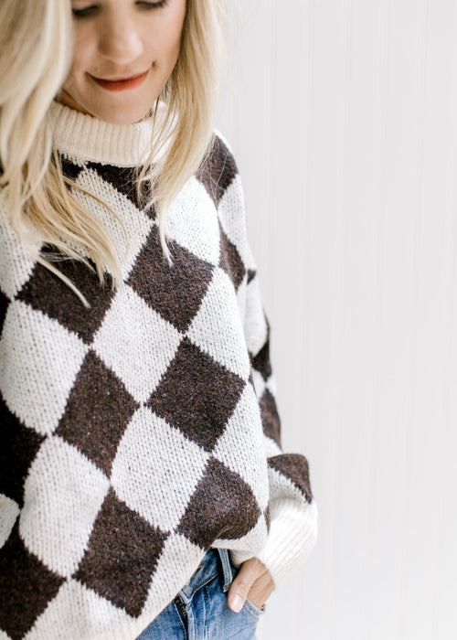 Model wearing a brown and white diamond pattern sweater with a round ribbed neck and long sleeves. 