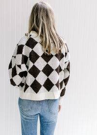 Back view of Model wearing a brown and white diamond pattern sweater with long sleeves.