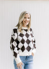 Model wearing jeans with a brown and white diamond pattern sweater with long sleeves. 