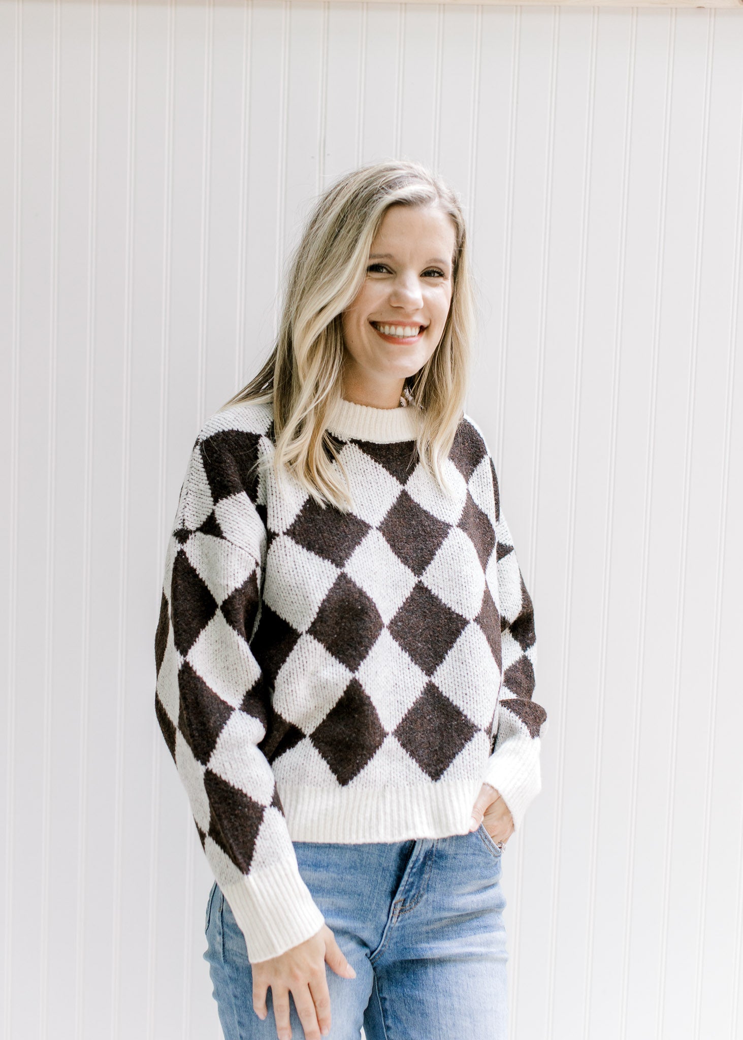 Model wearing jeans with a brown and white diamond pattern sweater with long sleeves. 