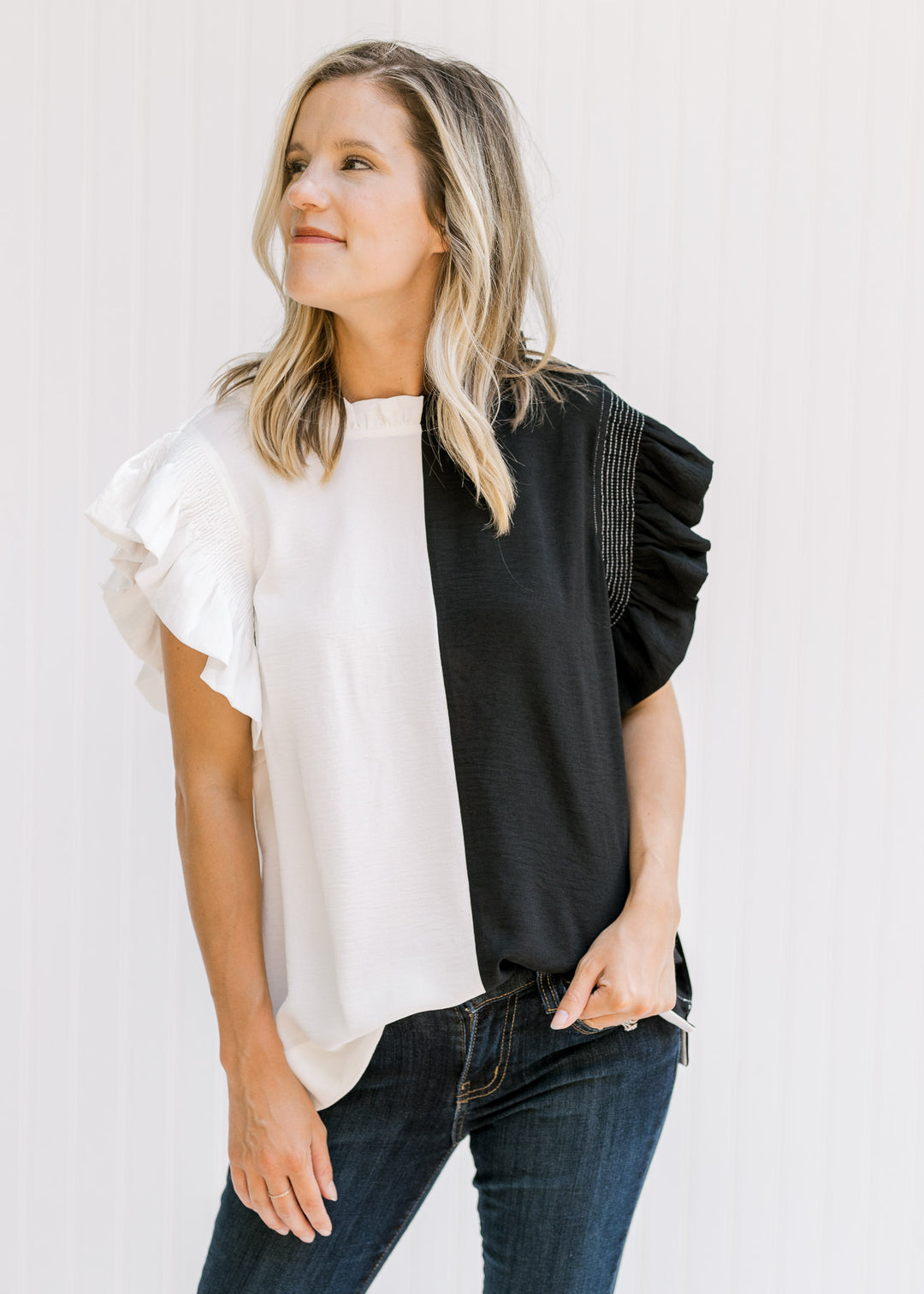 Model wearing jeans with a black and white colorblock top with cap sleeves and a keyhole closure. 