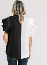 Back view of Model wearing a black and white colorblock top with flutter cap sleeves and a keyhole.