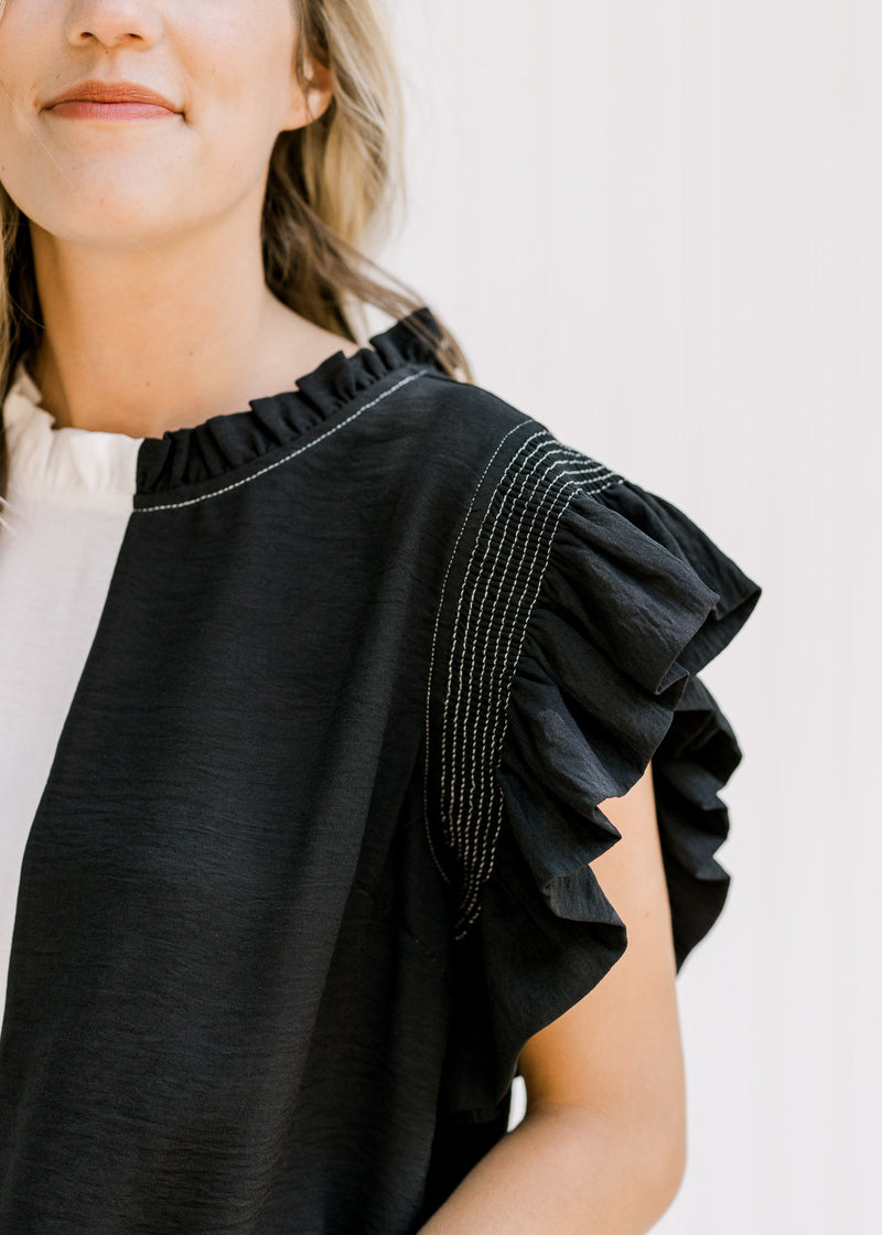 Close up view of black flutter capped sleeve on a black and white colorblock top. 