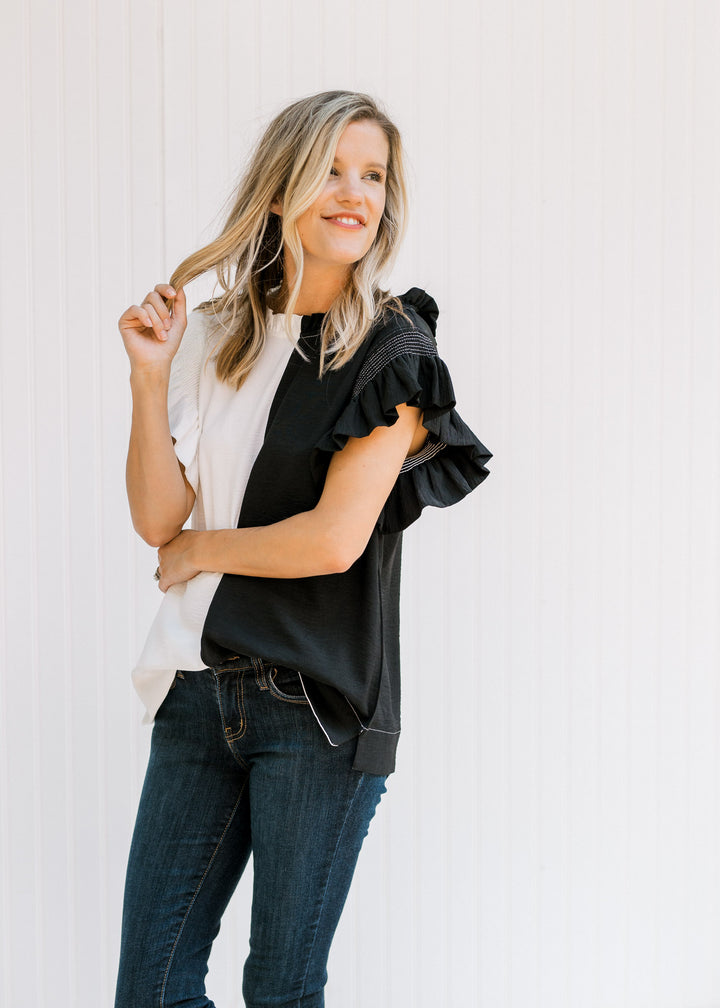 Model wearing a black and white colorblock top with flutter cap sleeves and a keyhole closure. 