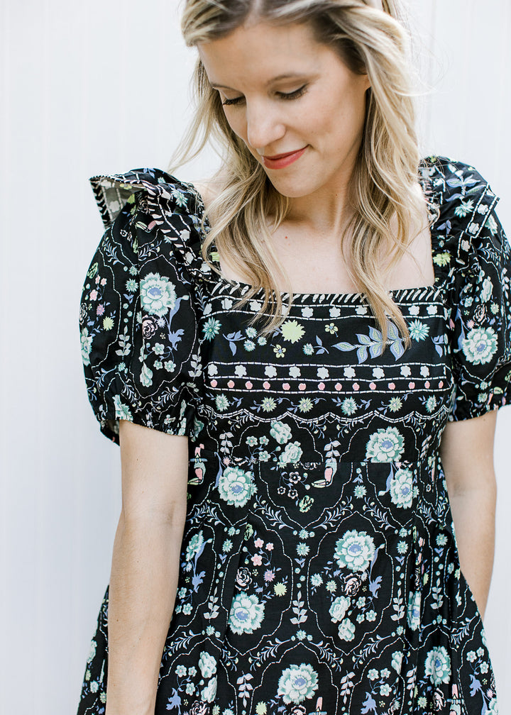Model wearing a square neck, black maxi with framed floral, empire waist and short sleeves.