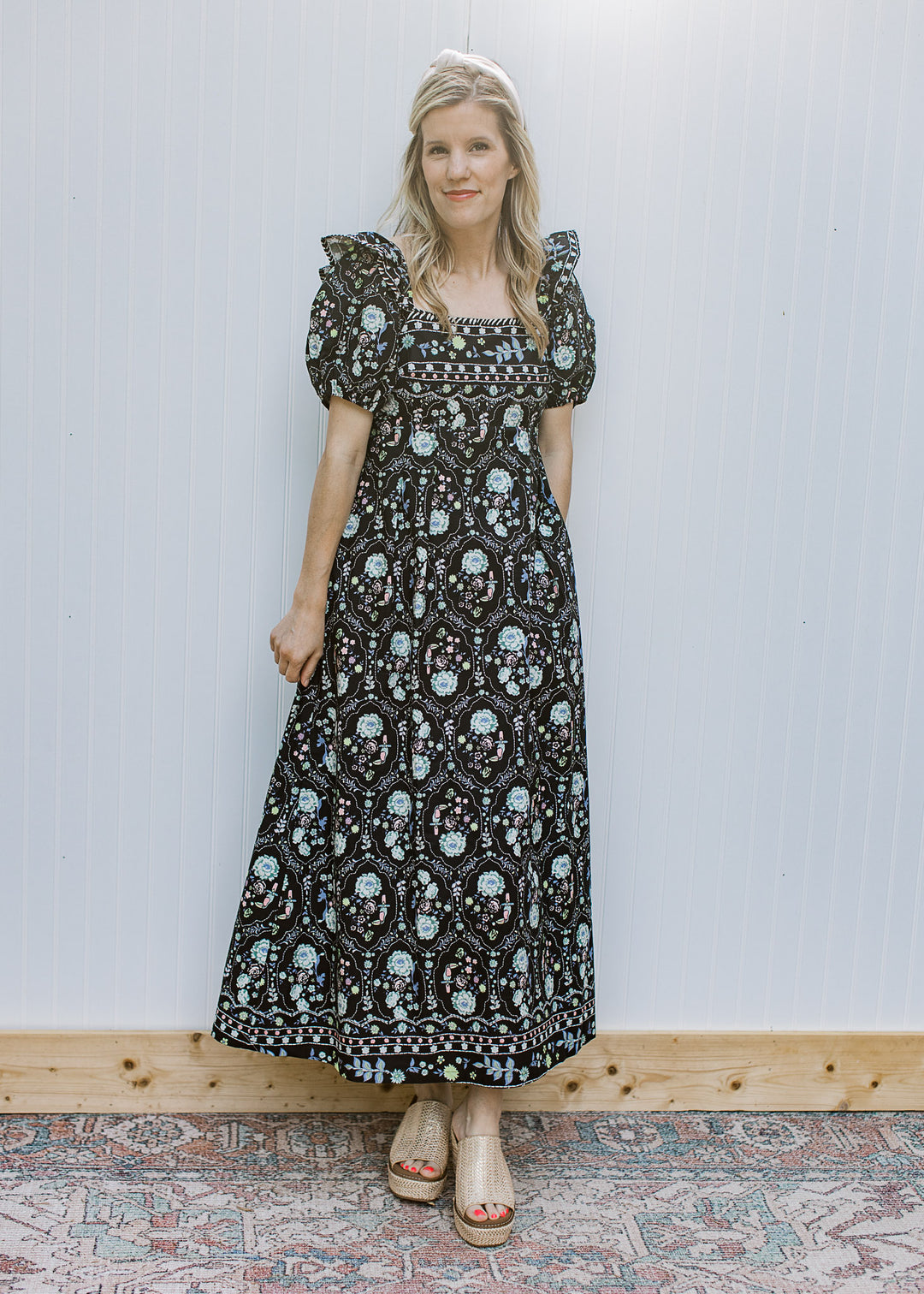 Model wearing a square neck, black maxi with floral, double ruffle at shoulder and short sleeves.