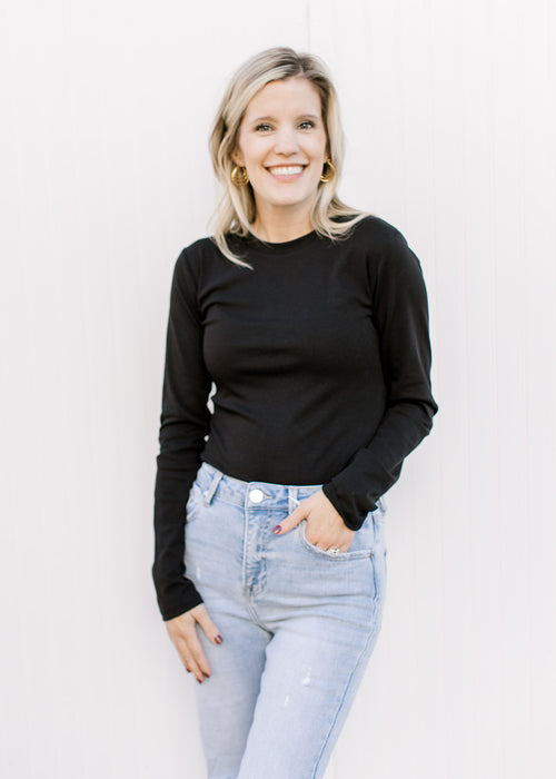 Model wearing a black long sleeve bodysuit with a round neck and two snap closure. 