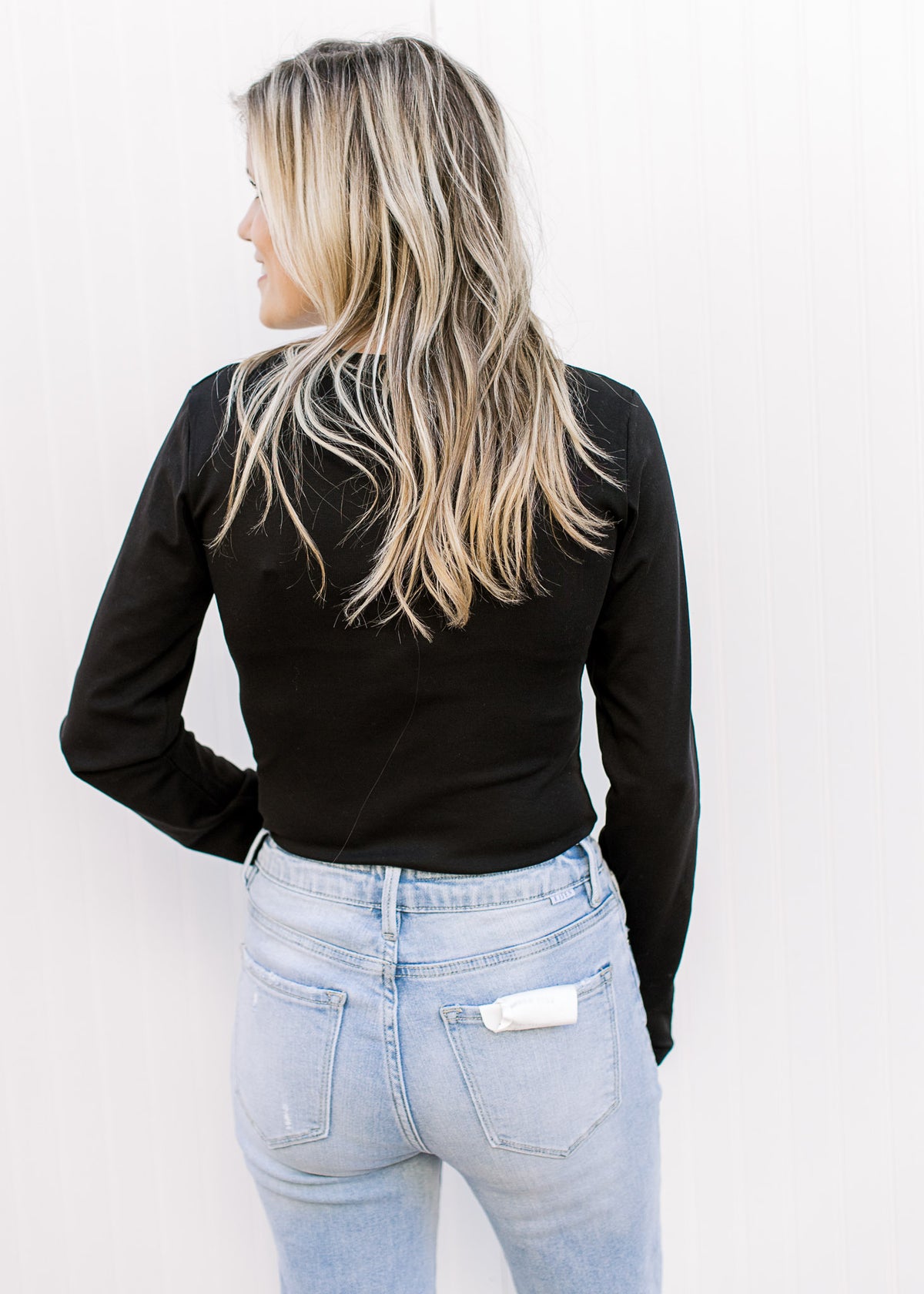 Back view of Model wearing a black long sleeve bodysuit with a round neck and two snap closure. 