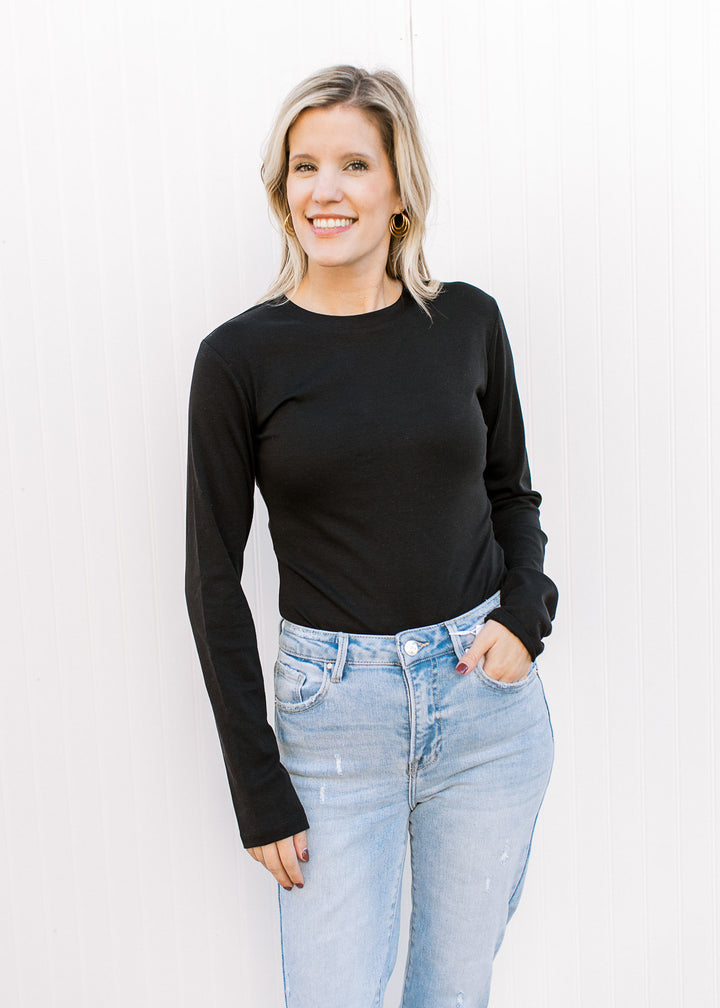 Model wearing jeans and a black long sleeve bodysuit with a round neck and two snap closure. 