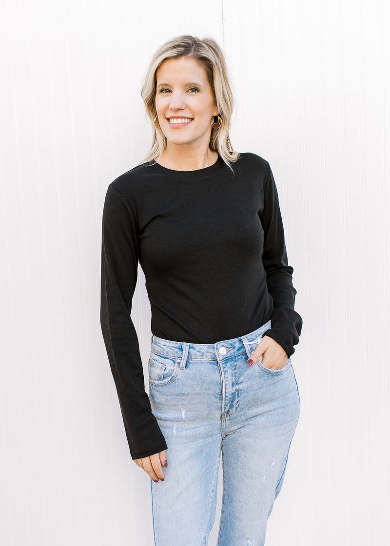 Model wearing jeans and a black long sleeve bodysuit with a round neck and two snap closure. 
