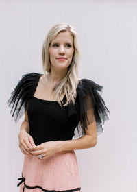 Model wearing a black bodysuit with a square neck and mesh ruffle sleeves. 