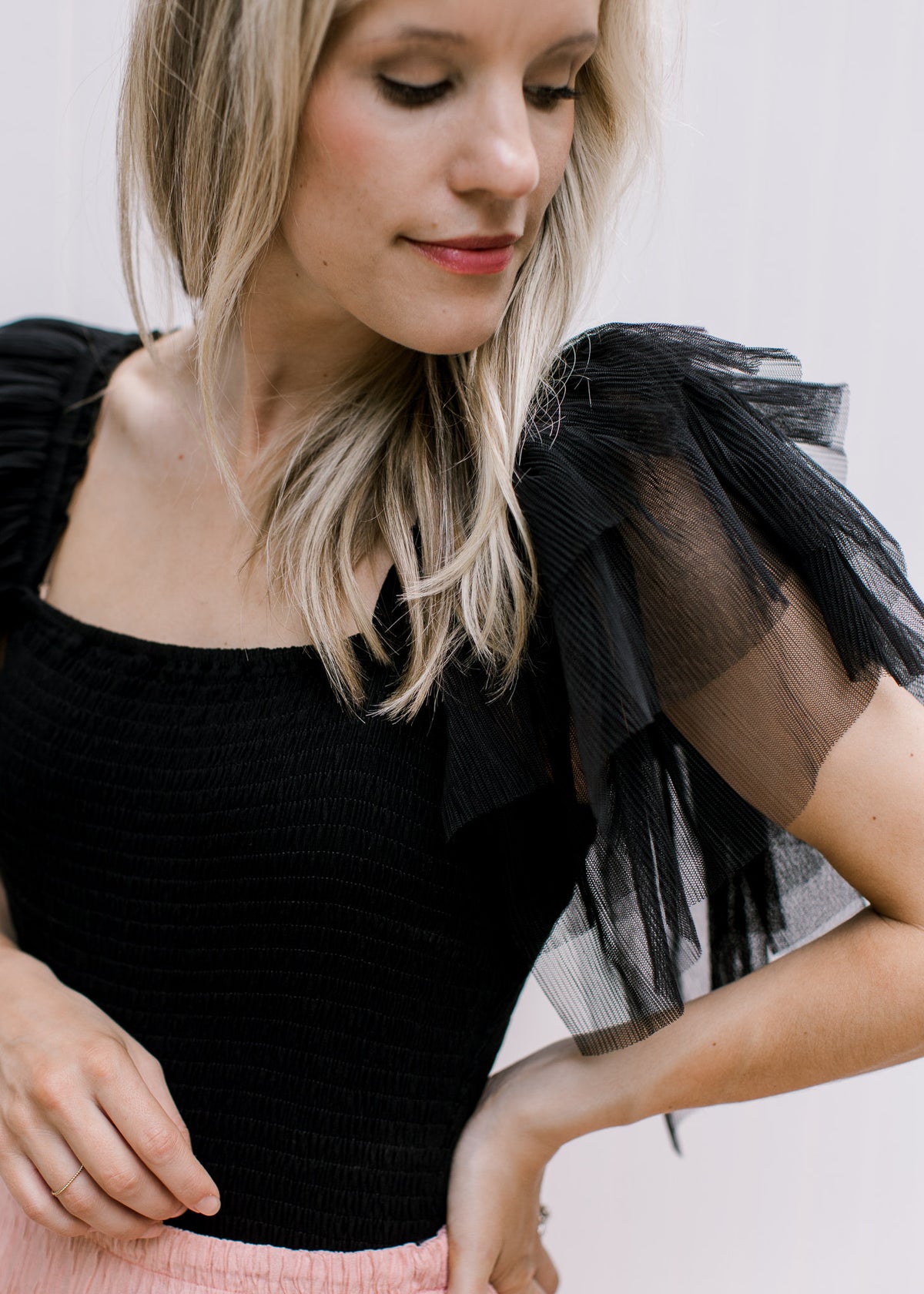 Close up of mesh ruffle sleeves on a black bodysuit with a square neck and double button closure. 