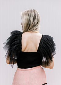 Back view of Model wearing a black bodysuit with a square neck and mesh ruffle sleeves.