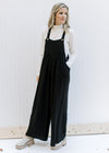 Model wearing a black jumpsuit with two button adjustable straps and wide leg pants. 