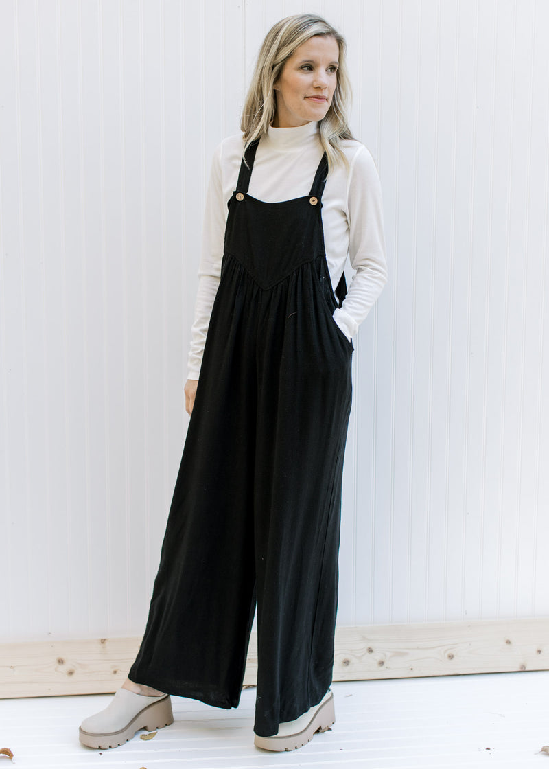 Model wearing a black jumpsuit with two button adjustable straps and wide leg pants. 
