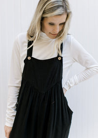 Model wearing a white top with a black jumpsuit wit adjustable straps and wide leg pants. 