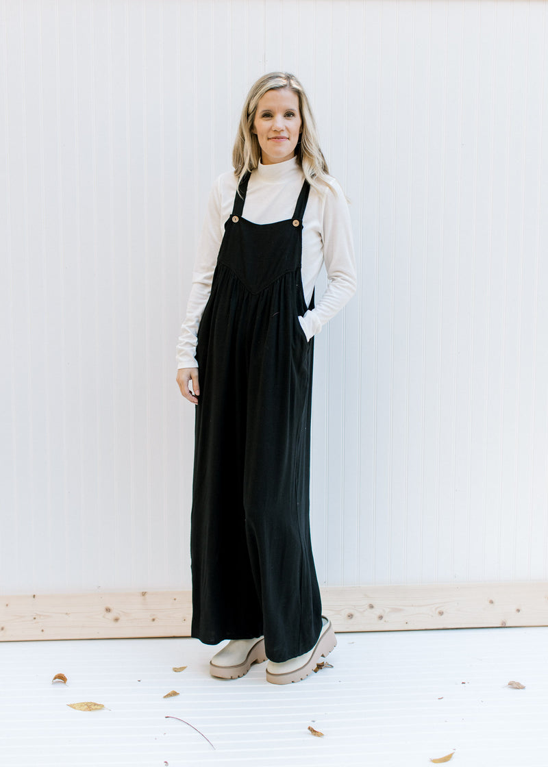 Model wearing a white top, mules and a black jumpsuit with adjustable straps and wide leg pants. 