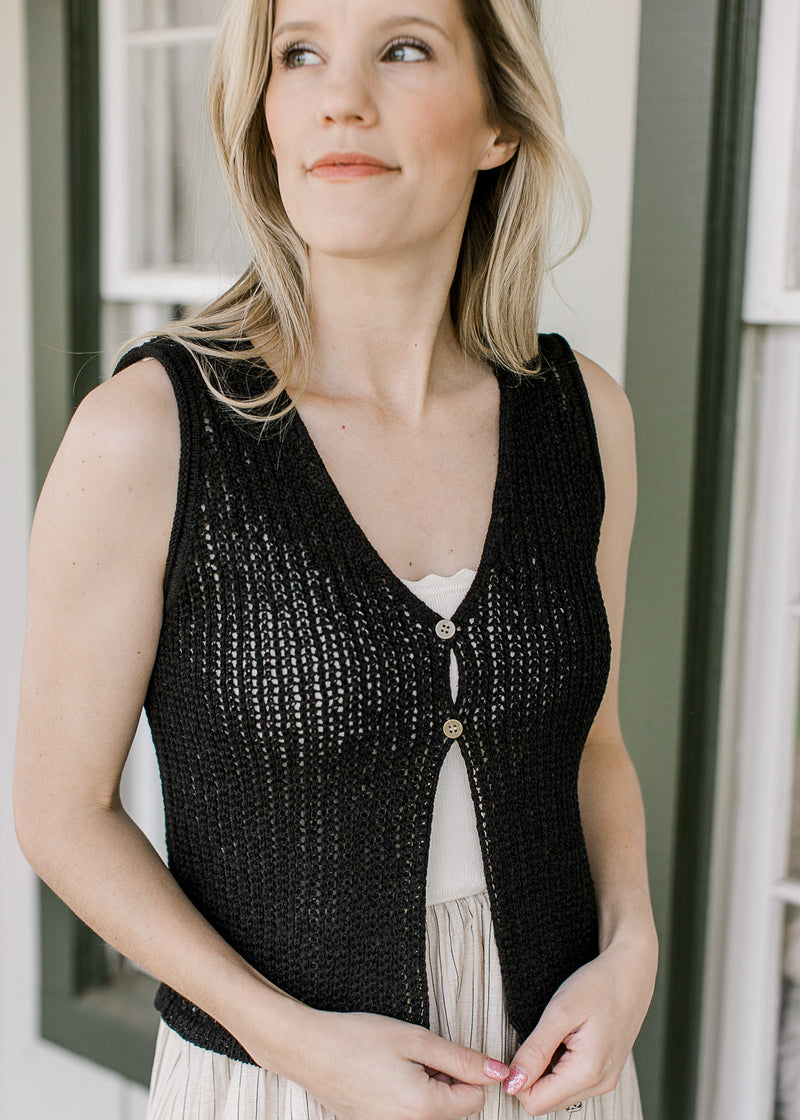 Model wearing a midi with a black vest with knit material, two button closure and a v-neck. 