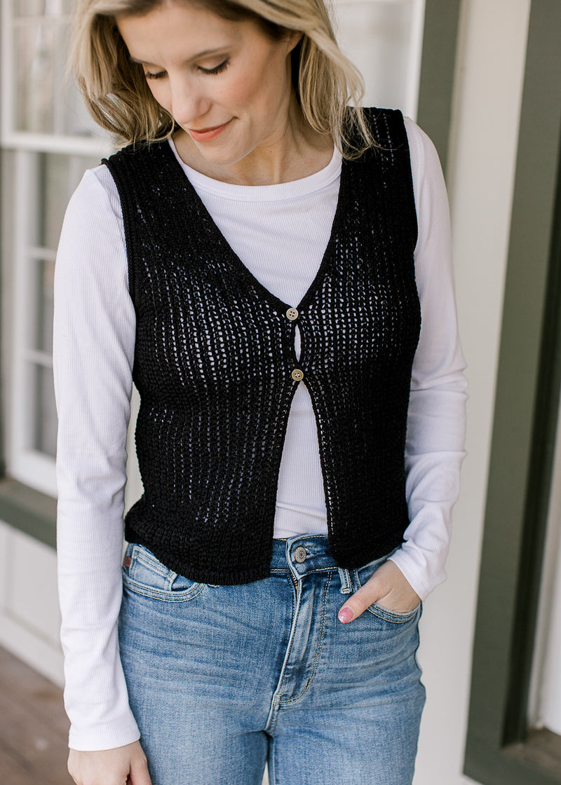 Model wearing a white top, jeans and a black knit vest with two button closure and a v-neck. 