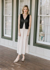 Model wearing a black vest over a sleeveless midi dress with a taupe skirt and black stripes.