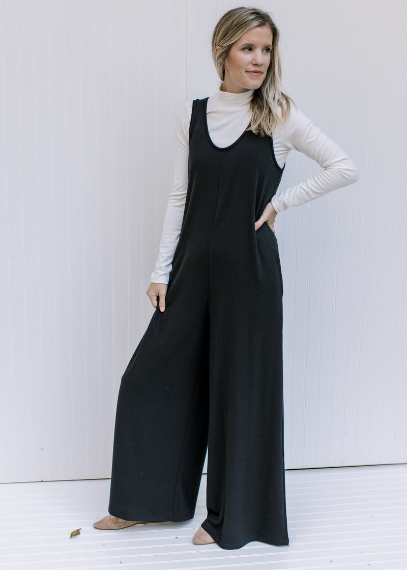 Model wearing white top and a black wide leg jumpsuit with a round neck and pockets. 