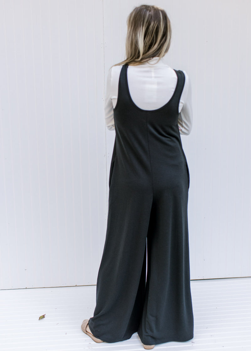 Back view of Model wearing white top and a black wide leg jumpsuit with a round neck and pockets. 