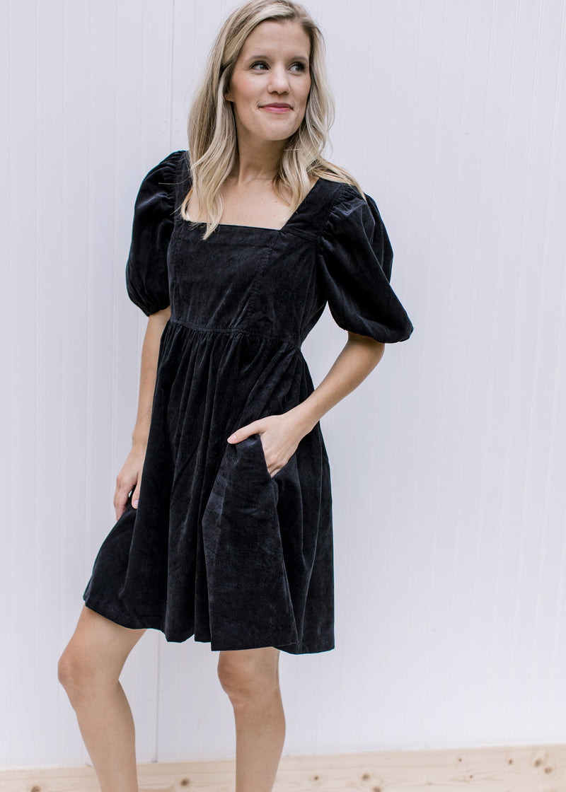Model wearing a black square neck dress with a babydoll cut, short puff sleeves and pockets. 