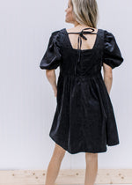 Back view of tie back and bubble short sleeves on an above the knee black dress with a babydoll cut.