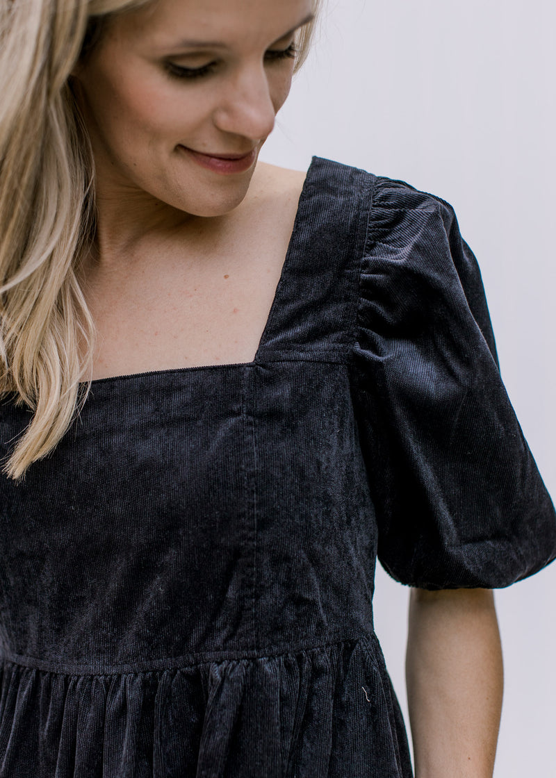 Close up on square neckline and bubble short sleeves on a black above the knee dress.