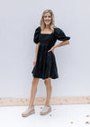 Model wearing mules with a black square neck dress with a babydoll cut and short puff sleeves. 