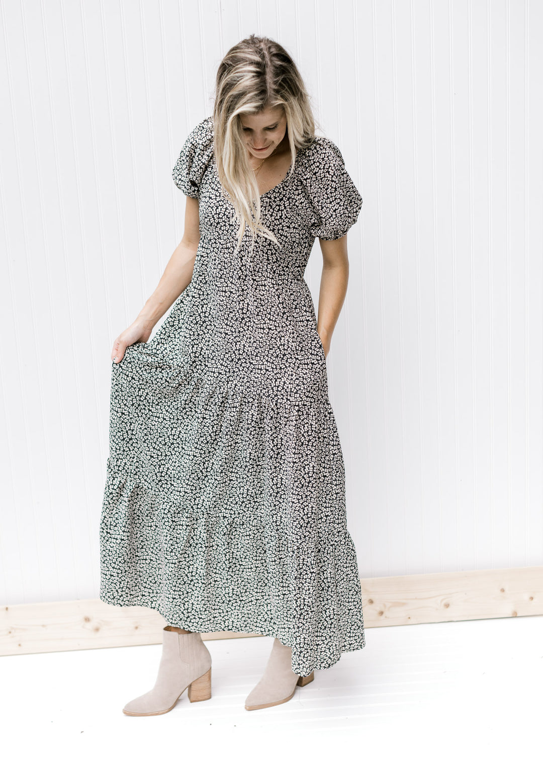 Model is wearing a black v-neck dress with white daisies, bubble short sleeves and tiered bottom. 