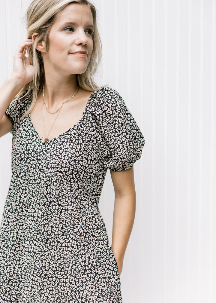Close up of v-neck and bubble short sleeves on a black dress with a white daisy pattern. 