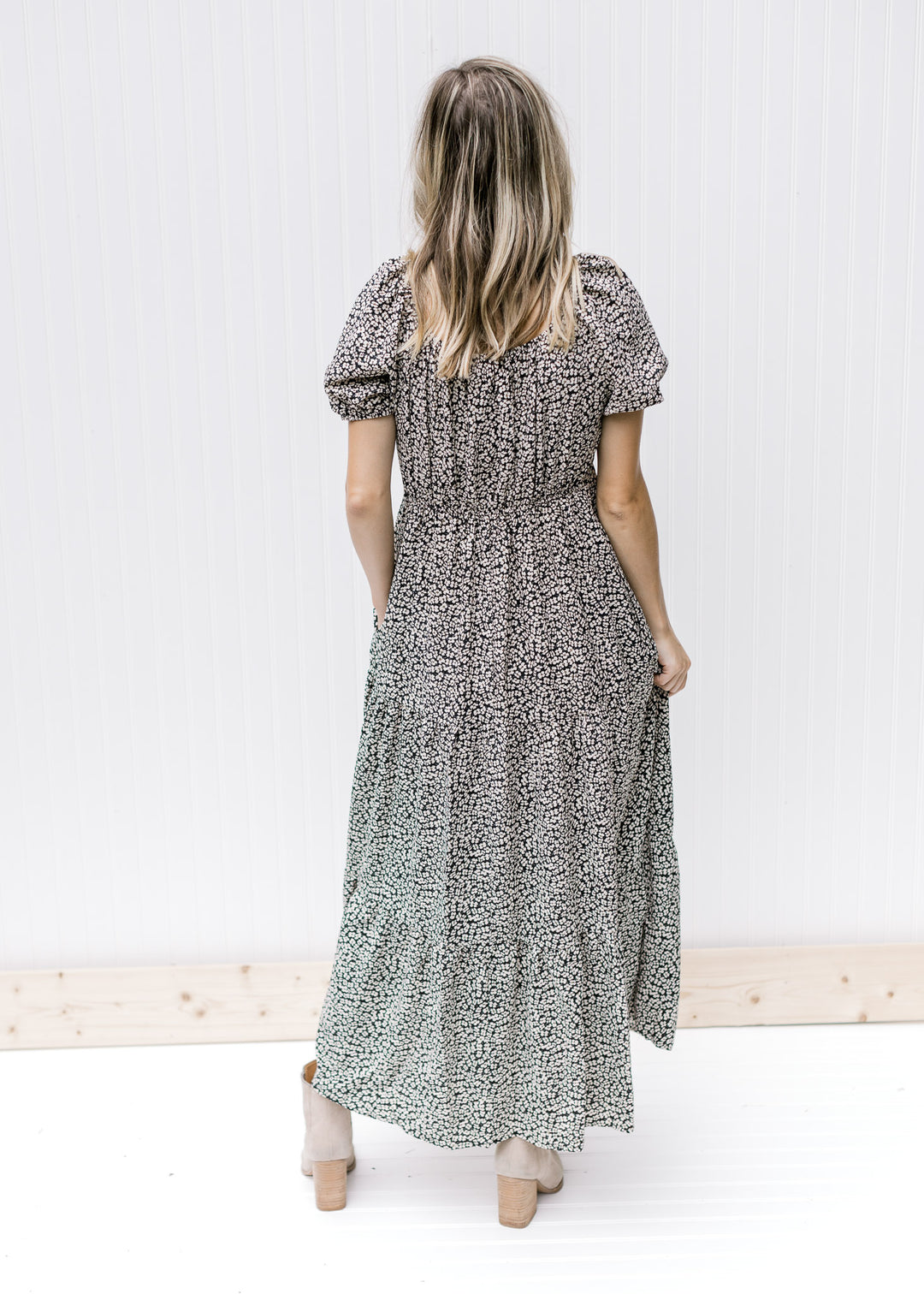 Back view of Model is wearing a black v-neck dress with white daisies and bubble short sleeves.