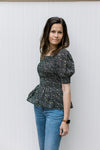 Model wearing jeans with a black peplum top with ditsy floral, square neck and bubble short sleeves.