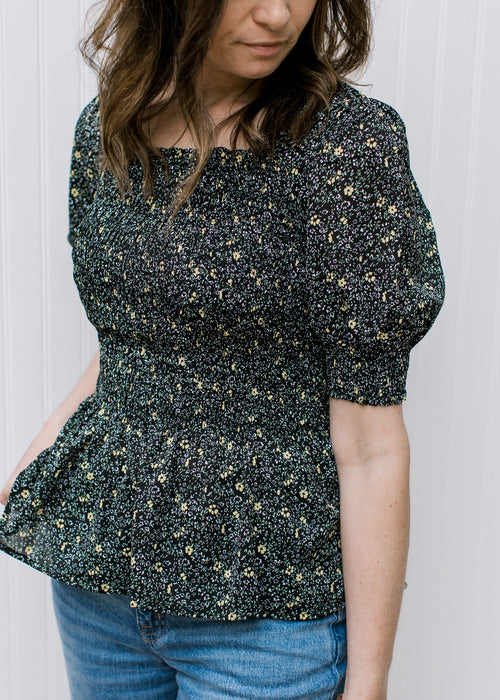 Model wearing a black peplum top with ditsy floral, square neck and bubble short sleeves. 