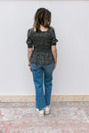 Back view of Model wearing a black peplum top with ditsy floral, square neck and short sleeves.