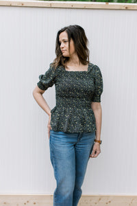 Model wearing a black peplum top with ditsy floral, smocked bodice and bubble short sleeves.