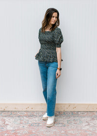 Model wearing jeans, wedges and a black peplum top with ditsy floral, square neck and short sleeves.