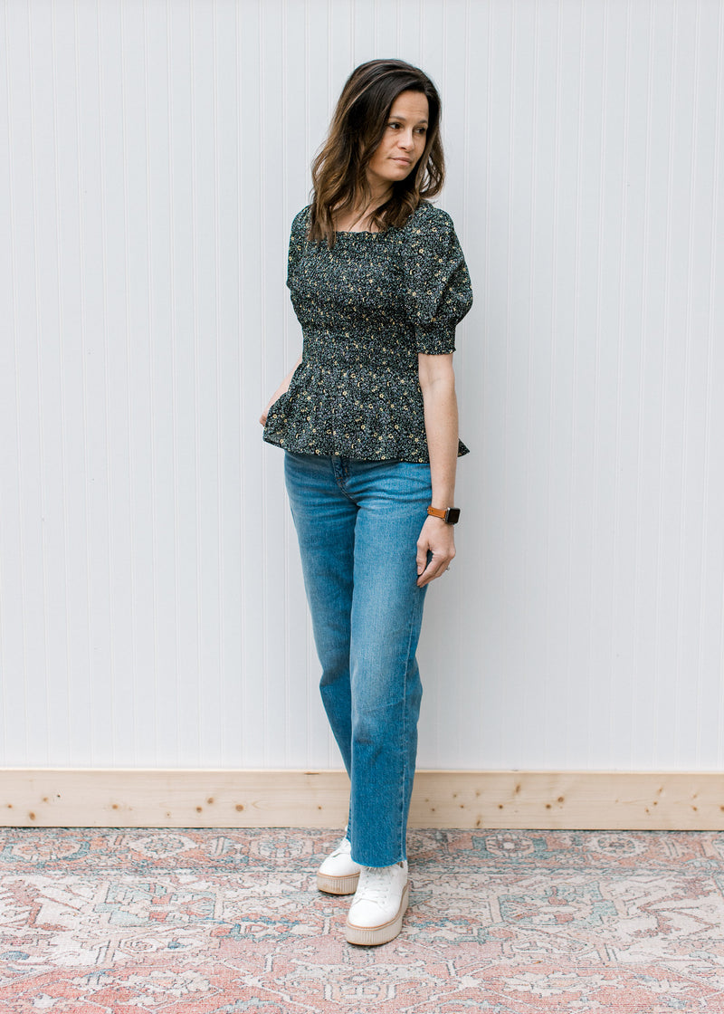 Model wearing jeans, wedges and a black peplum top with ditsy floral, square neck and short sleeves.