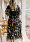 Back view of Model wearing a black dress with neutral flowers and bubble short sleeves. 